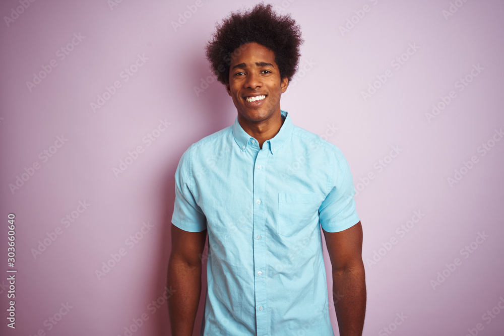 Young american man with afro hair wearing blue shirt standing over isolated pink background with a happy and cool smile on face. Lucky person. Young american man with afro hair wearing blue shirt standing over isolated pink background with a happy and cool smile on face. Lucky person.