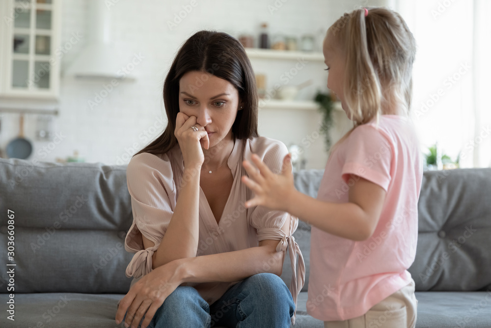 Stressed thoughtful 30s mother ignoring playful happy small daughter. Stressed thoughtful 30s mother ignoring playful happy small daughter.