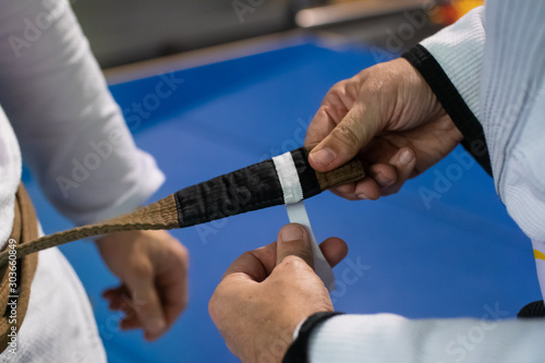 Promotion during brazilian jiu jitsu training. Close up photo of trainer's hand adding a white stripe to adept's brown belt.