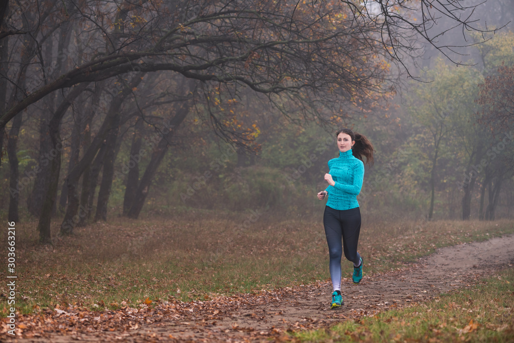 Woman jogging alone through misty forest in autumn