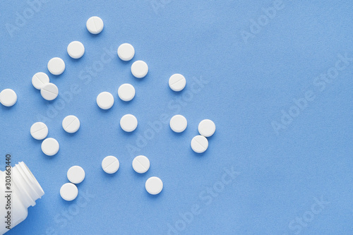 Bottle with white vitamin pills scattered on a blue background.