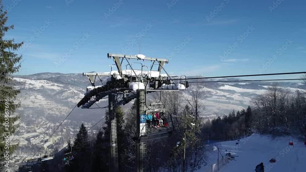Aerial view of ski resort and Ski lift ropeway on highland alpine mountain winter resort on bright sunny day. Ski chairlift cable way with people enjoy skiing and snowboarding. Aerial view of ski resort and Ski lift ropeway on highland alpine mountain winter resort on bright sunny day. Ski chairlift cable way with people enjoy skiing and snowboarding.