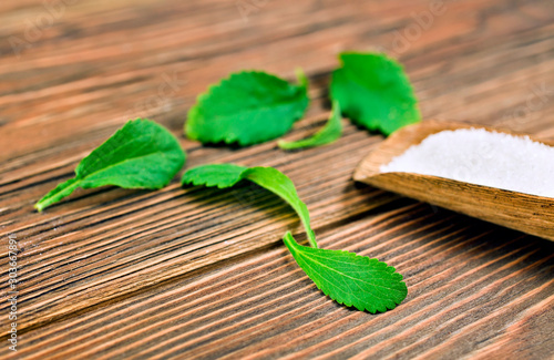 Stevia leaves with sugar in a wooden scoop on a wooden background.