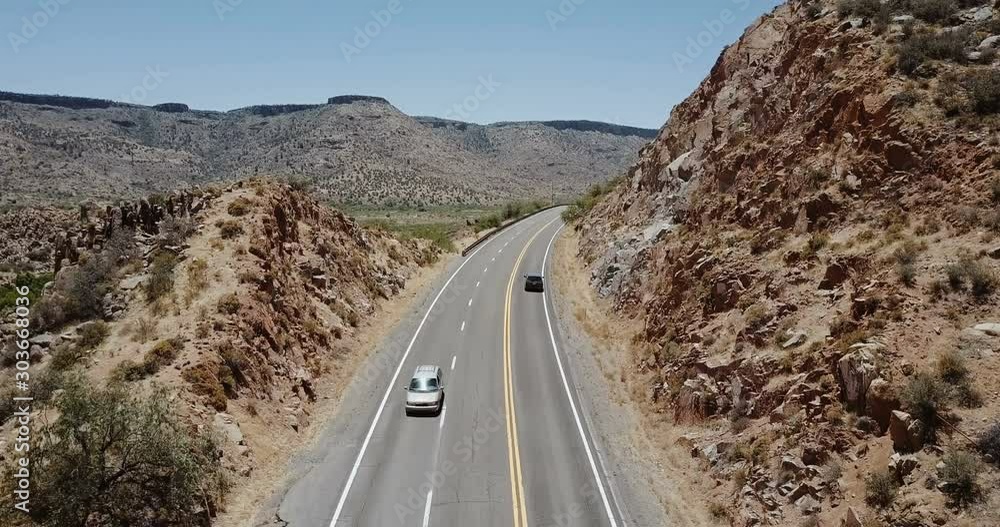 Drone following minivan car driving along majestic desert rock hills on ...