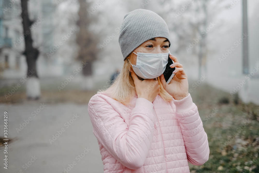 Plakat A young girl is standing near the road in a medical mask. Protection against a virus epidemic in a city.