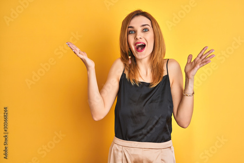 Redhead caucasian business woman standing over yellow isolated background celebrating crazy and amazed for success with arms raised and open eyes screaming excited. Winner concept
