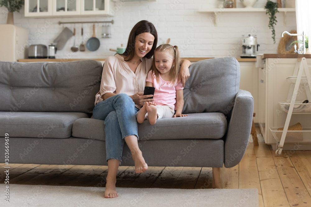 Happy 30s woman looking at cellphone screen with adorable daughter.