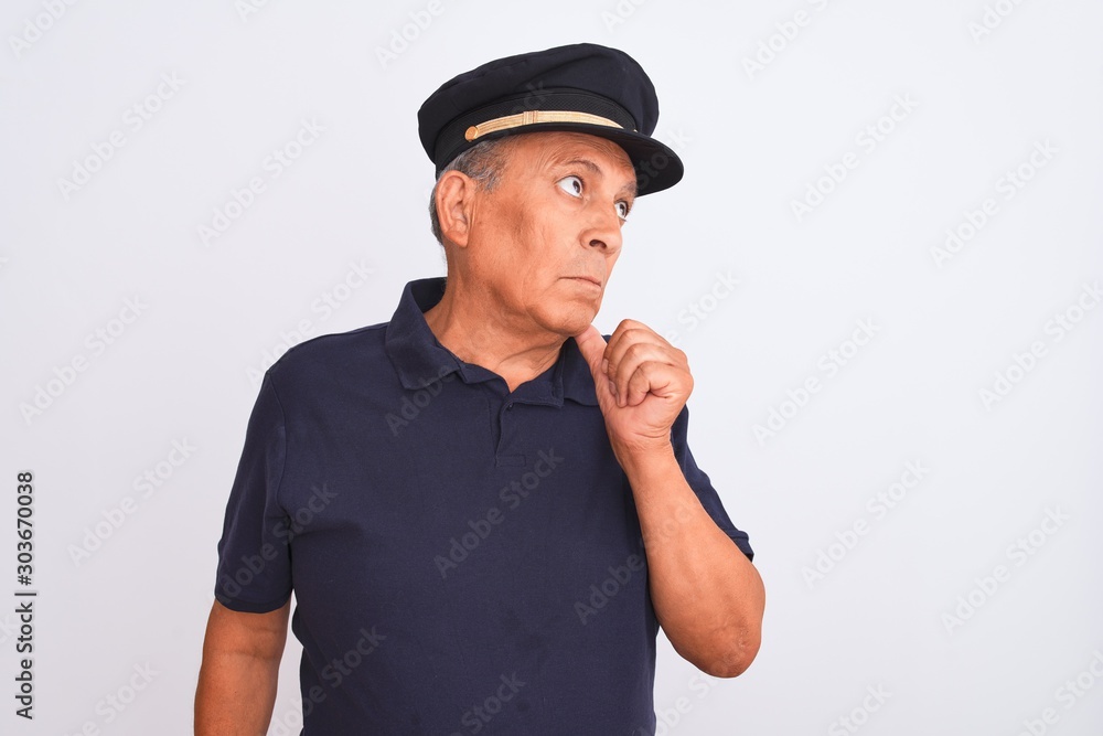 Senior grey-haired man wearing black polo and captain hat over isolated white background with hand on chin thinking about question, pensive expression. Smiling with thoughtful face. Doubt concept. Senior grey-haired man wearing black polo and captain hat over isolated white background with hand on chin thinking about question, pensive expression. Smiling with thoughtful face. Doubt concept.