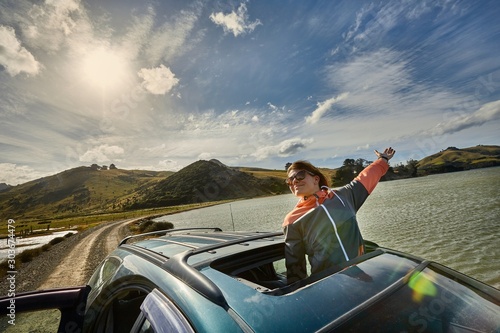 Woman leaning out through the sunroof of a car on a countryside journey on Otago Peninsula, New Zealand © Gudellaphoto