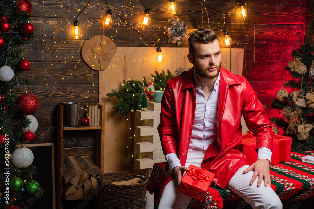 Sexy hot boy wearing red christmas jacket and holding christmas present in  his hand. Christmas time. Present box. Shopping sale. Bearded handsome man  at full christmas decorated interior. – Stock-Foto | Adobe