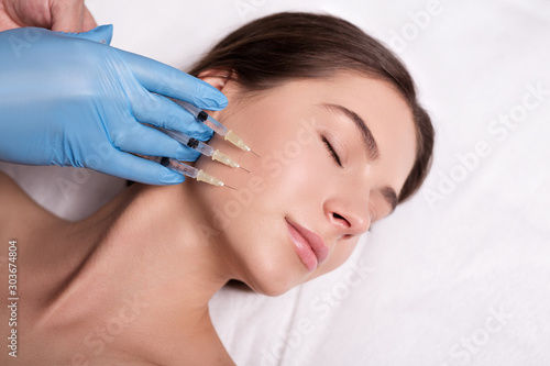 Beauty Injection. Closeup Of Doctor Hands With Syringe Near Female Face. Portrait Of Beautiful Woman Receiving Facial Skin Lifting Treatment.