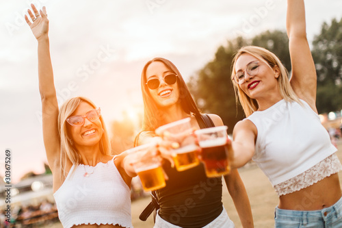 Three female friends cheering with beer at music festival