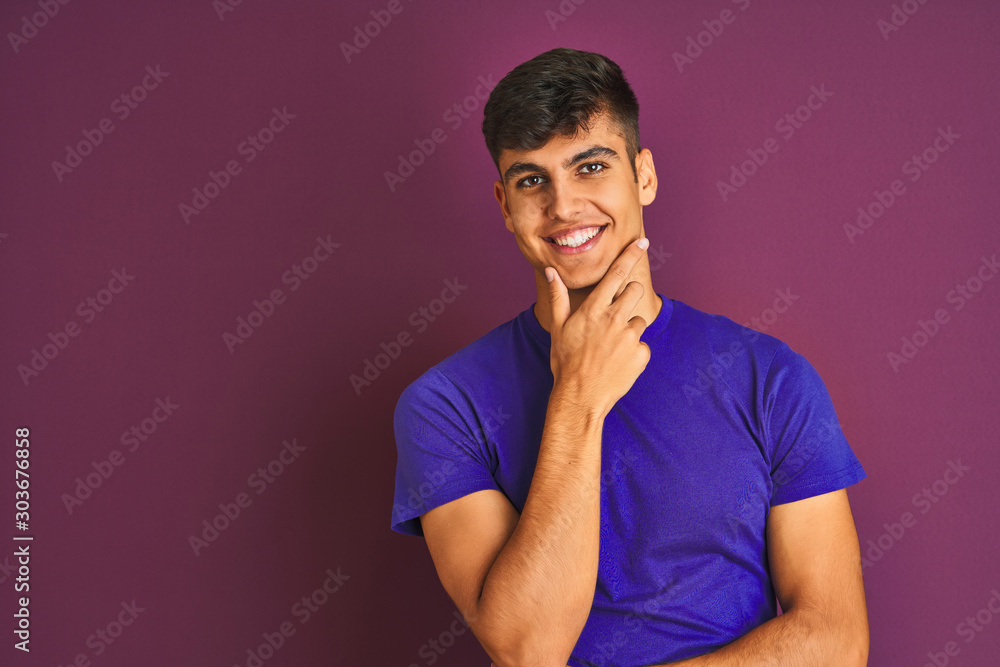 Young indian man wearing t-shirt standing over isolated purple background looking confident at the camera smiling with crossed arms and hand raised on chin. Thinking positive. Young indian man wearing t-shirt standing over isolated purple background looking confident at the camera smiling with crossed arms and hand raised on chin. Thinking positive.