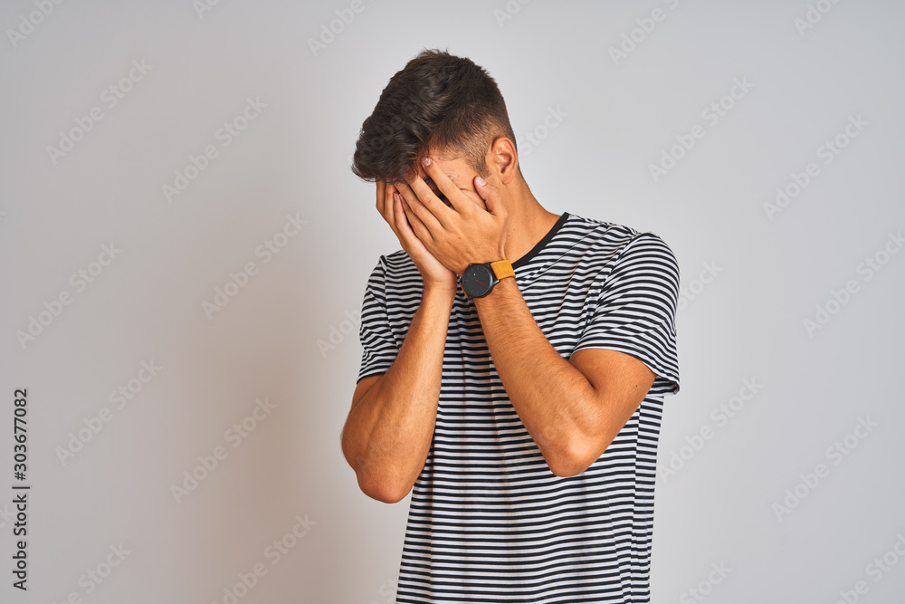 Photos Young indian man wearing navy striped t-shirt standing over isolated white background with sad expression covering face with hands while crying