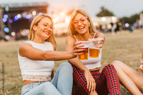 Girls sitting on the ground and cheering with beer at music festival
