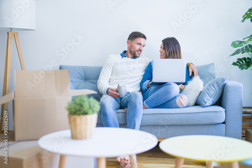 Young beautiful couple sitting on the sofa drinking cup of coffee using laptop at new home around cardboard boxes © Krakenimages.com