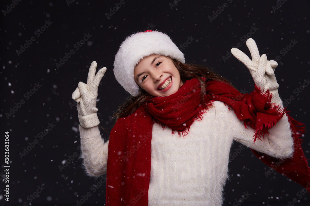 Portrait of young beautiful smiling girl in red Santa hat with white snowflakes on a dark background. Xmas fashion model with long curly hair. Winter holidays, Christmas, New Year concept Portrait of young beautiful smiling girl in red Santa hat with white snowflakes on a dark background. Xmas fashion model with long curly hair. Winter holidays, Christmas, New Year concept