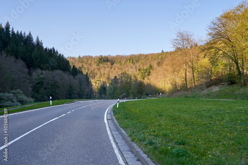 Beautiful spring landscape with a road between trees, sunny day and blue sky in the German forest Schwarzwald