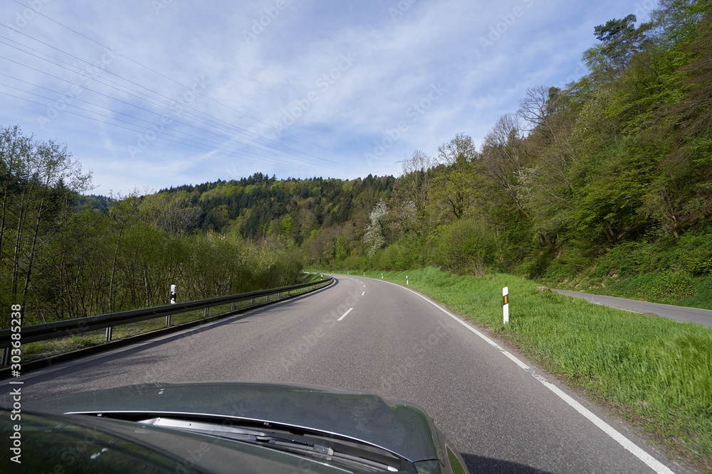 Photo from the window of a car that rides on a road with turns along the forest Schwarzwald, Germany. Car hood and forest road