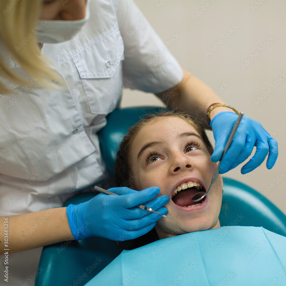 Dentist doing teeth checkup of little girl at medical clinic. Health care and stomatology medicine concept. Dentist doing teeth checkup of little girl at medical clinic. Health care and stomatology medicine concept.