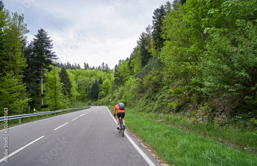 A highway through a forest with turns and a cyclist rides along it. Schwarzwald forest road and cyclist. Germany