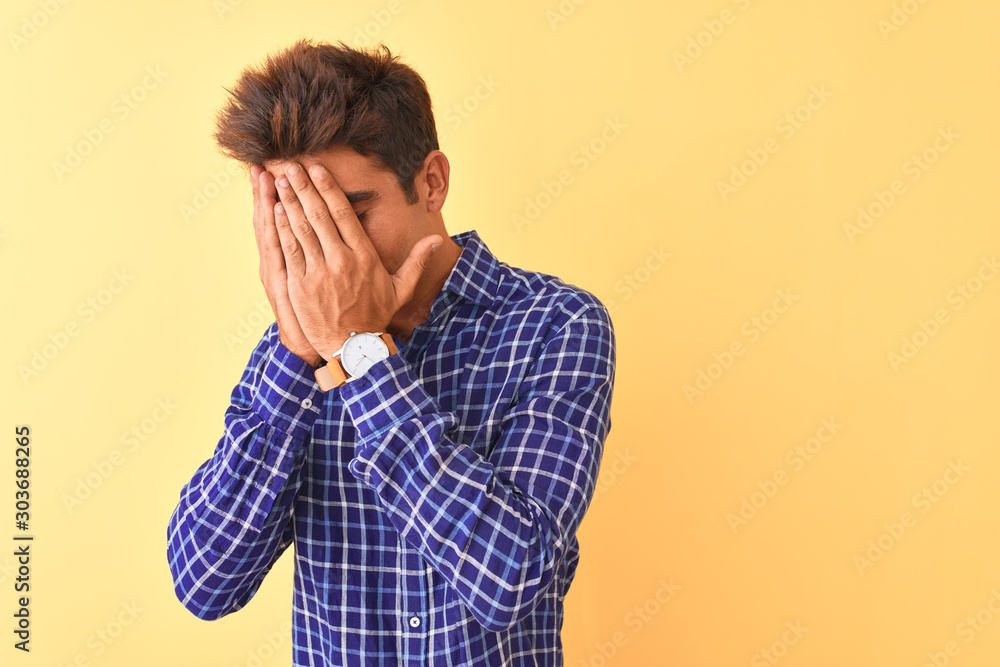 Young handsome man wearing casual shirt standing over isolated yellow background with sad expression covering face with hands while crying. Depression concept. Young handsome man wearing casual shirt standing over isolated yellow background with sad expression covering face with hands while crying. Depression concept.