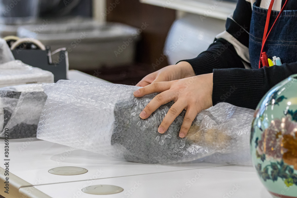 Φωτογραφία Female vendor hands wrapping a product with bubble film protective at a store's counter, indoors