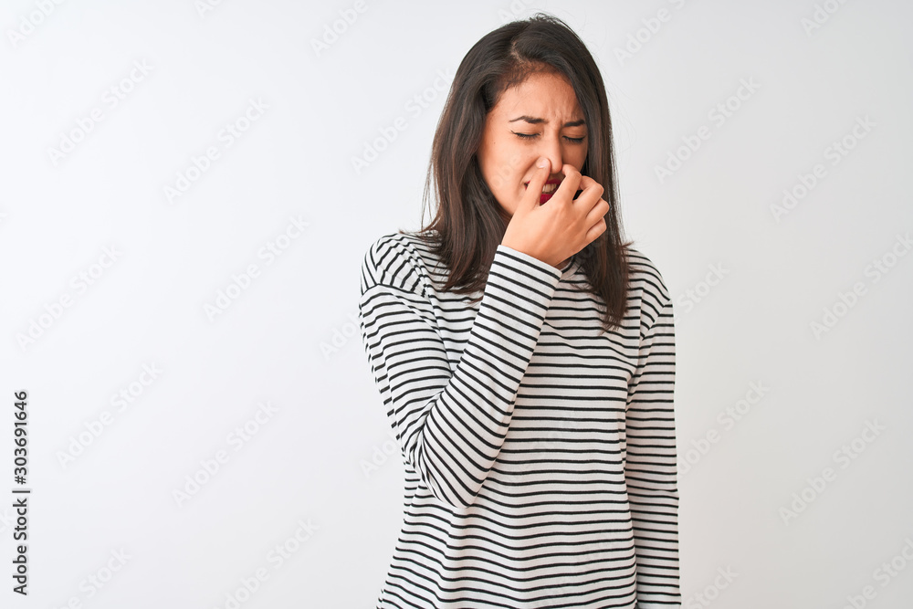 Young beautiful chinese woman wearing striped t-shirt standing over isolated white background smelling something stinky and disgusting, intolerable smell, holding breath with fingers on nose. Young beautiful chinese woman wearing striped t-shirt standing over isolated white background smelling something stinky and disgusting, intolerable smell, holding breath with fingers on nose.