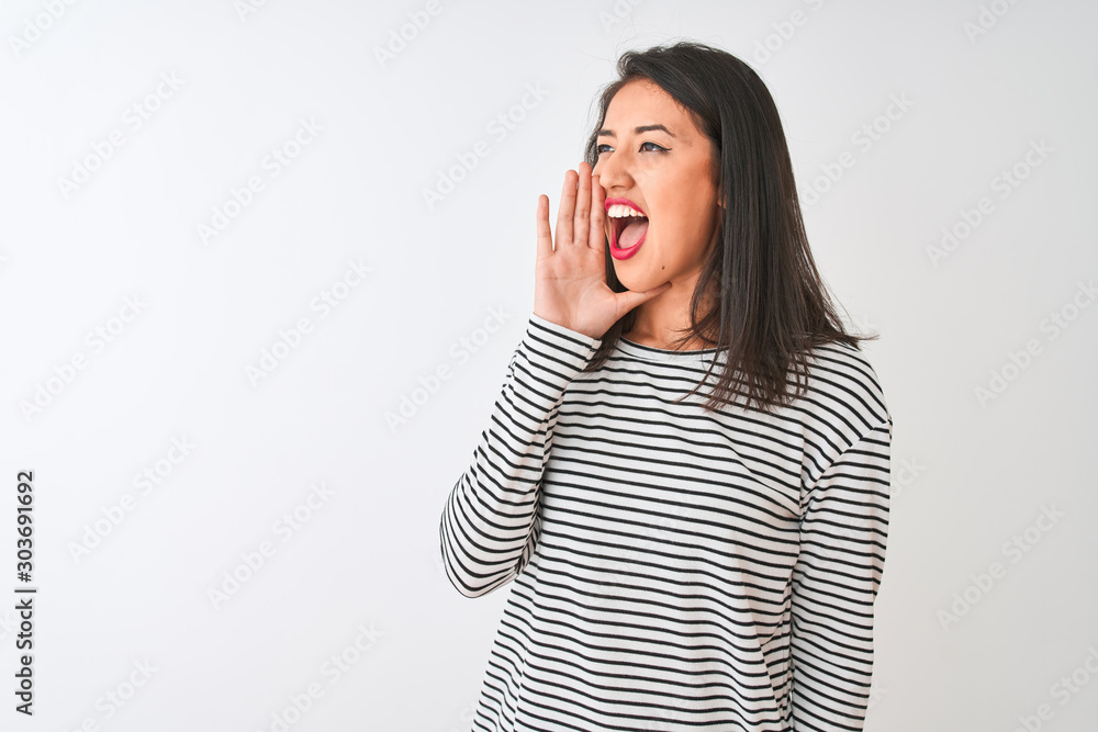 Young beautiful chinese woman wearing striped t-shirt standing over isolated white background shouting and screaming loud to side with hand on mouth. Communication concept. Young beautiful chinese woman wearing striped t-shirt standing over isolated white background shouting and screaming loud to side with hand on mouth. Communication concept.