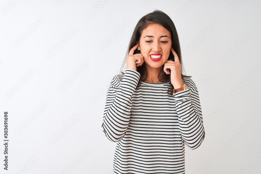 Young beautiful chinese woman wearing striped t-shirt standing over isolated white background covering ears with fingers with annoyed expression for the noise of loud music. Deaf concept. Young beautiful chinese woman wearing striped t-shirt standing over isolated white background covering ears with fingers with annoyed expression for the noise of loud music. Deaf concept.