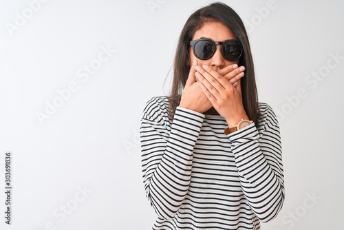 Chinese woman wearing striped t-shirt and sunglasses standing over isolated white background shocked covering mouth with hands for mistake. Secret concept. © Krakenimages.com