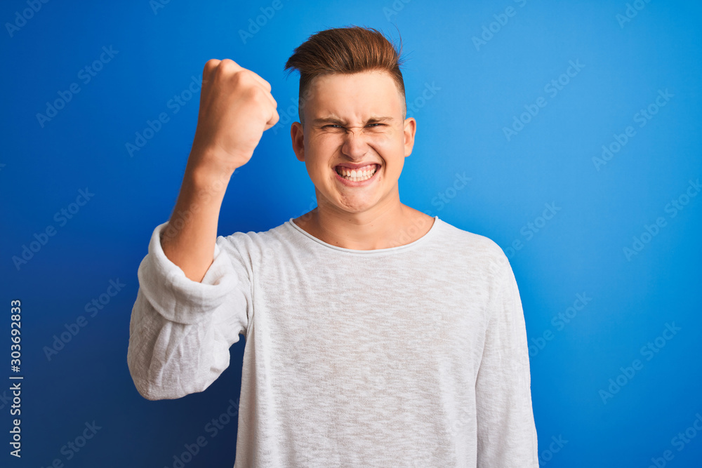 Young handsome man wearing white casual t-shirt standing over isolated blue background annoyed and frustrated shouting with anger, crazy and yelling with raised hand, anger concept Young handsome man wearing white casual t-shirt standing over isolated blue background annoyed and frustrated shouting with anger, crazy and yelling with raised hand, anger concept
