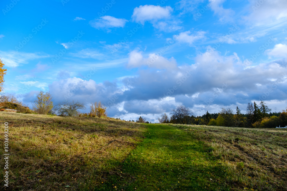 Field on a hill under a crooked blue sky with white clouds