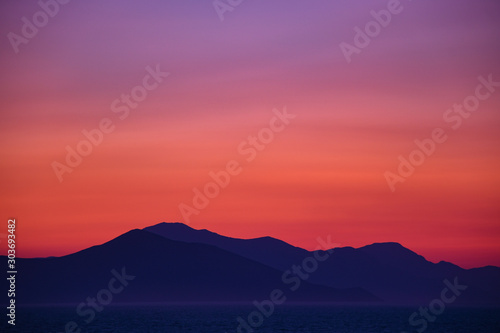 Beautiful colorful sunset seen from the island surrounded with sea over the high mainland hills 