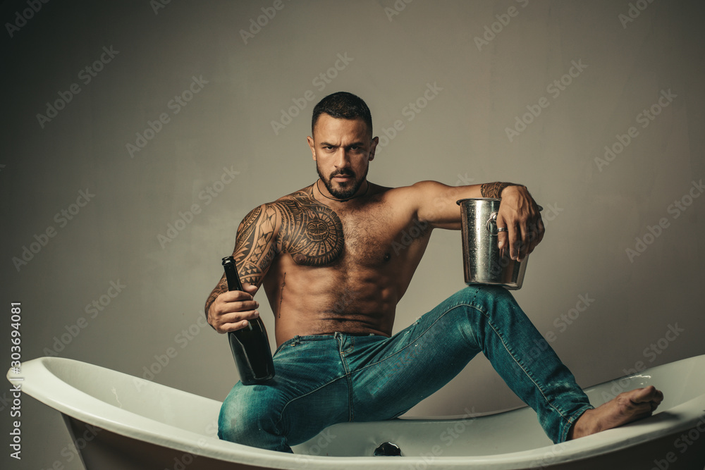Stockfoto Handsome bearded shirtless man in jeans with sexy body in bathroom.  Sexual macho man in bath. Strong muscular tattoed man holding champagne  bottle and posing in bathroom. | Adobe Stock