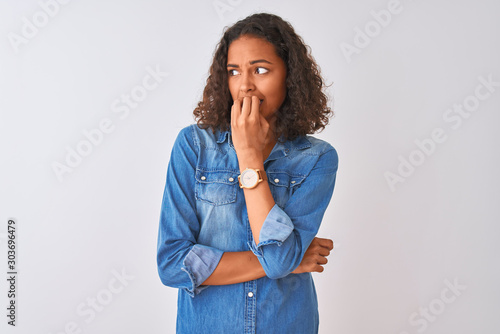 Young brazilian woman wearing denim shirt standing over isolated white background looking stressed and nervous with hands on mouth biting nails. Anxiety problem.
