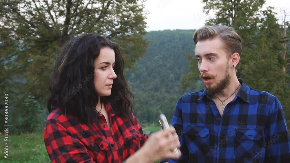 Young caucasian couple in casual clothes vape electronic cigarette near the forest in the autumn evening. Bad habit. Slow motion Young caucasian couple in casual clothes vape electronic cigarette near the forest in the autumn evening. Bad habit. Slow motion