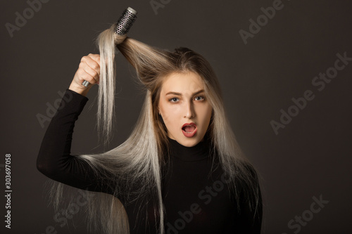 beautiful young woman with long hair on a black background combs her hair