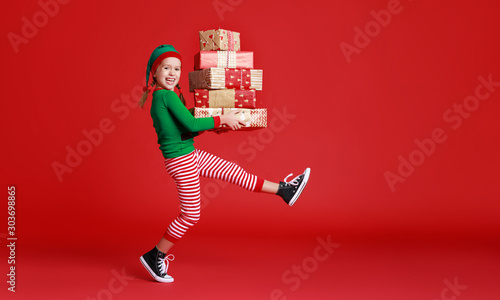 Cuadro en lienzo cheerful funny child in Christmas elf costume with gifts on   red background