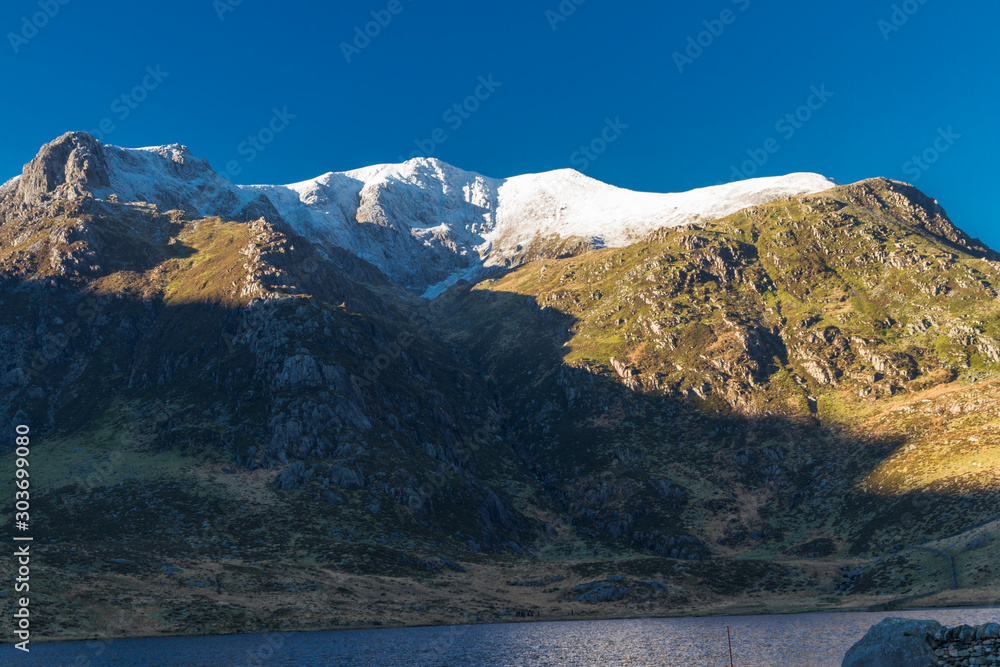 Early morning light and shadow over mountains and snow. Snow capped mountains, Y Garn, Lake or Llyn Idwal in foreground. Landscape