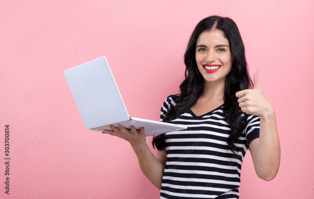 Young woman with a laptop computer giving thumb up on a pink background Young woman with a laptop computer giving thumb up on a pink background