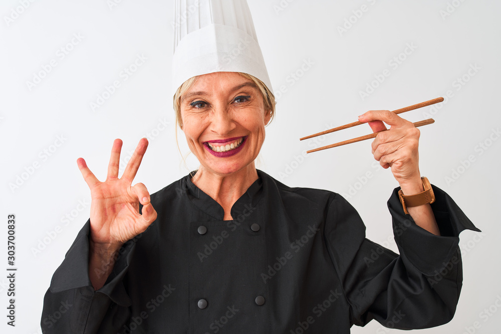 Middle age chef woman wearing cap holding chopsticks over isolated white background doing ok sign with fingers, excellent symbol Middle age chef woman wearing cap holding chopsticks over isolated white background doing ok sign with fingers, excellent symbol