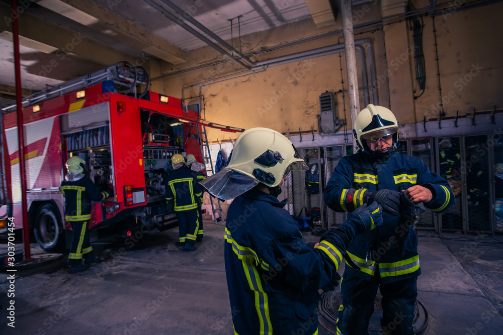 Firefighters preparing their uniform and the firetruck in the background inside the fire station Firefighters preparing their uniform and the firetruck in the background inside the fire station