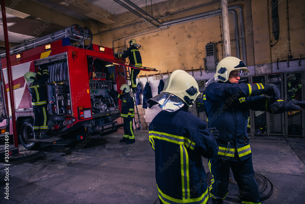 Firefighters preparing their uniform and the firetruck in the background inside the fire station Firefighters preparing their uniform and the firetruck in the background inside the fire station