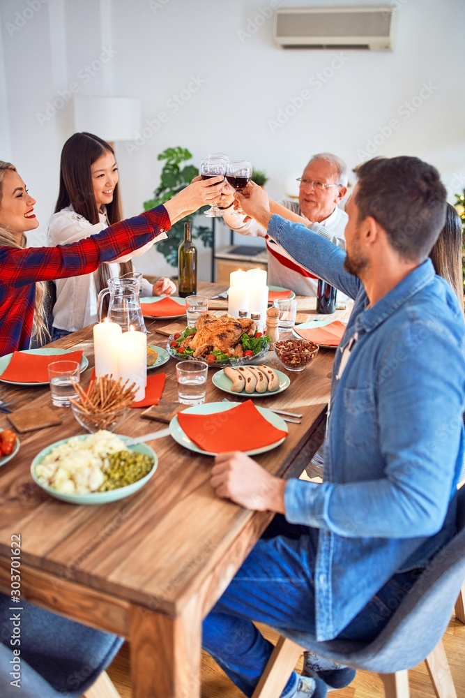 Beautiful group of people meeting smiling happy and confident. Eating roasted turkey and toasting with cup of wine celebrating Thanksgiving Day at home