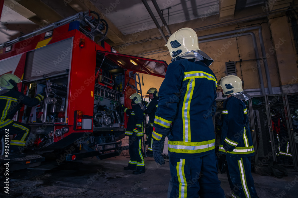 Firefighters preparing their uniform and the firetruck in the background inside the fire station Firefighters preparing their uniform and the firetruck in the background inside the fire station