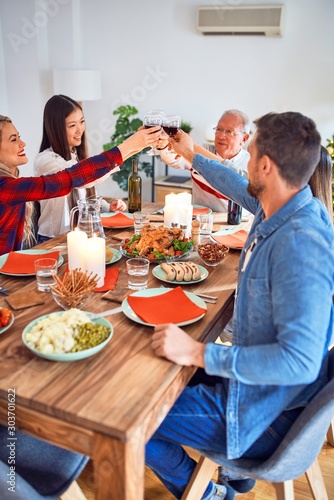 Beautiful group of people meeting smiling happy and confident. Eating roasted turkey and toasting with cup of wine celebrating Thanksgiving Day at home
