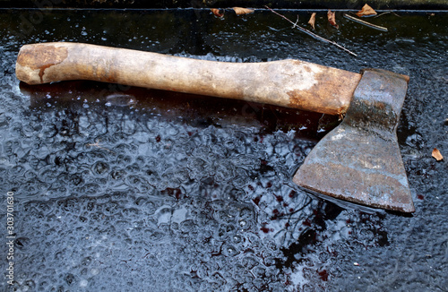 Autumn with an ax. A vintage working working ax with a birch handle, rust and notches lies on the ice surface.