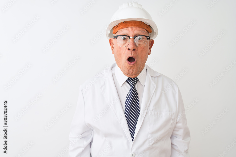 Senior grey-haired engineer man wearing coat and helmet over isolated white background afraid and shocked with surprise expression, fear and excited face. Senior grey-haired engineer man wearing coat and helmet over isolated white background afraid and shocked with surprise expression, fear and excited face.