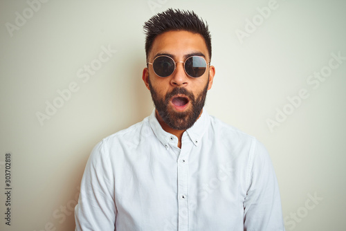 Handsome indian buinessman wearing shirt and sunglasses over isolated white background afraid and shocked with surprise expression, fear and excited face.